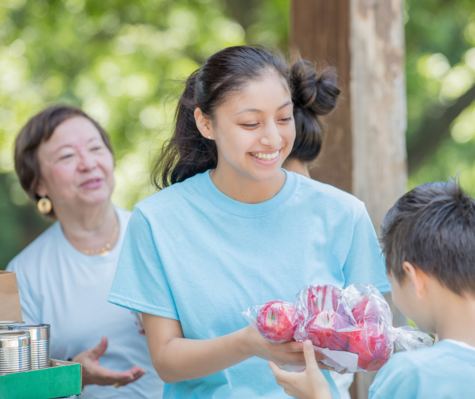 A young woman hands apples to a child at a community event.